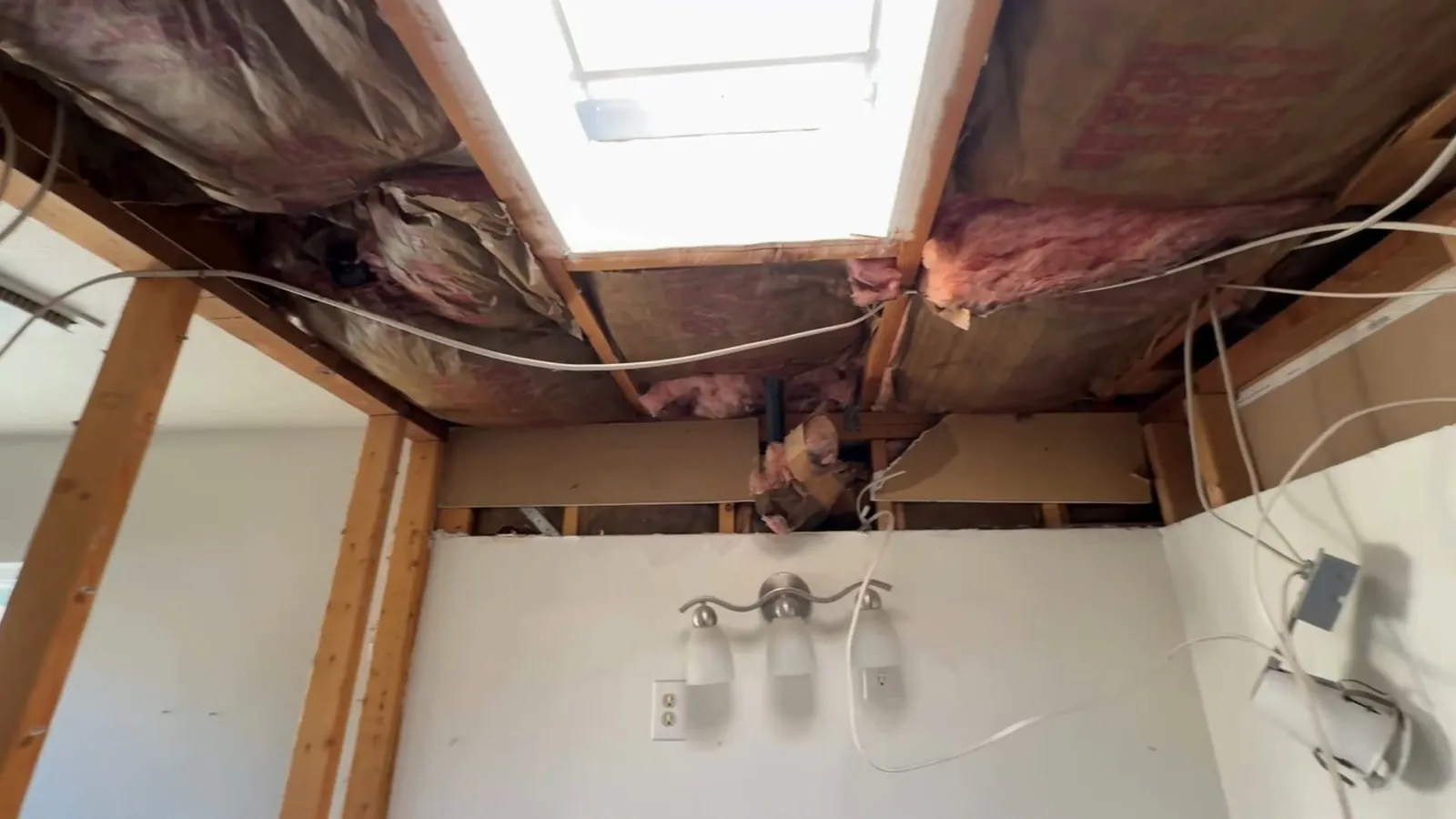 Bathroom ceiling opened up to the joists, with pink insulation and a skylight above.