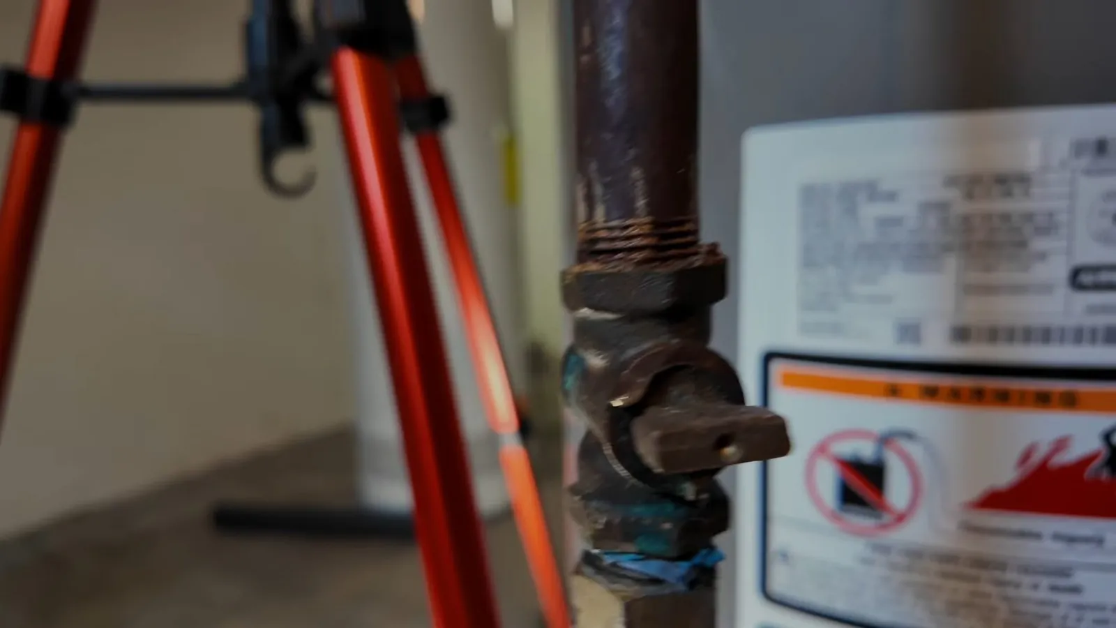 Brass valve beside a water heater label, with an orange tripod in the foreground.
