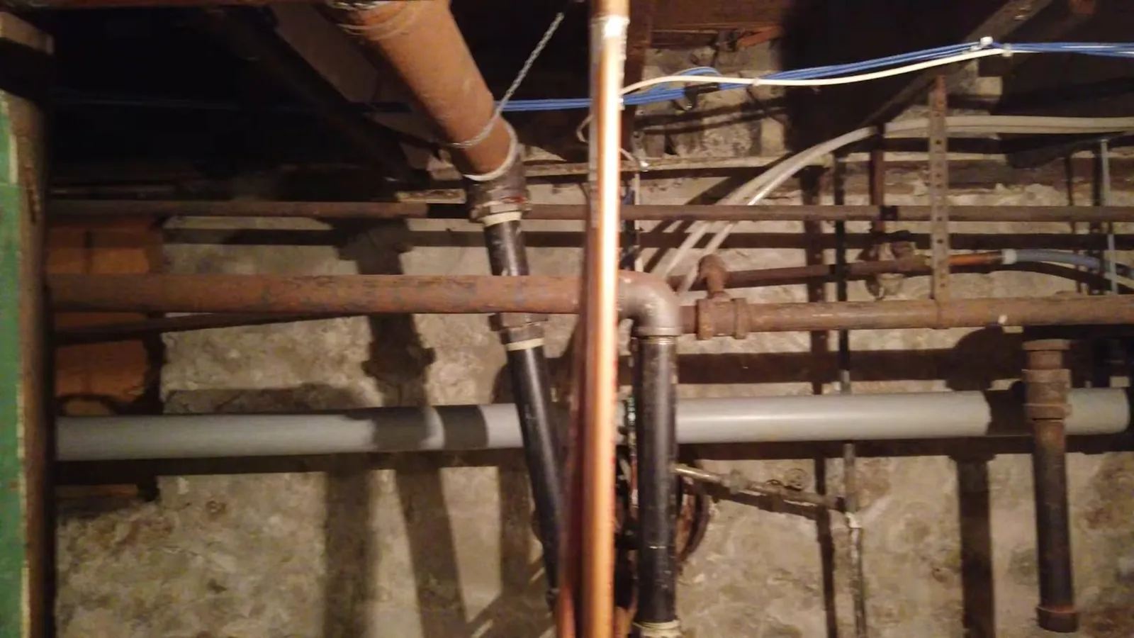 Basement ceiling with copper, galvanized and plastic pipes running under floor joists and insulation.
