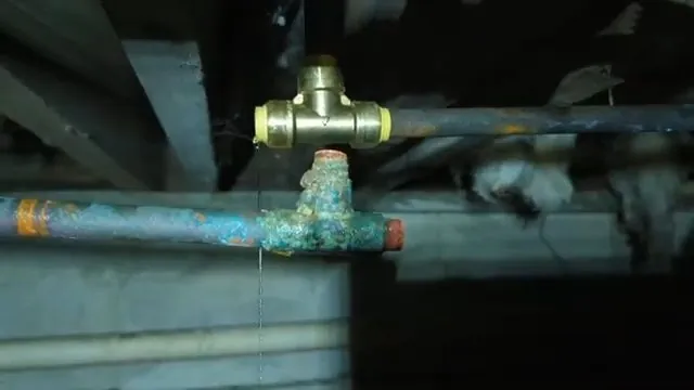 Blue-green corroded copper pipe next to a brass tee fitting under floor joists.
