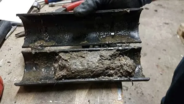 Cut open section of black drain pipe packed with sludge.