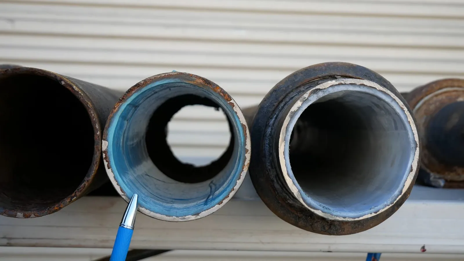 Three cut pipe ends side by side, one with a blue epoxy liner inside it.