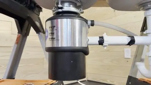 Garbage disposal mounted below a sink with a white drain pipe and a ribbed hose attached.