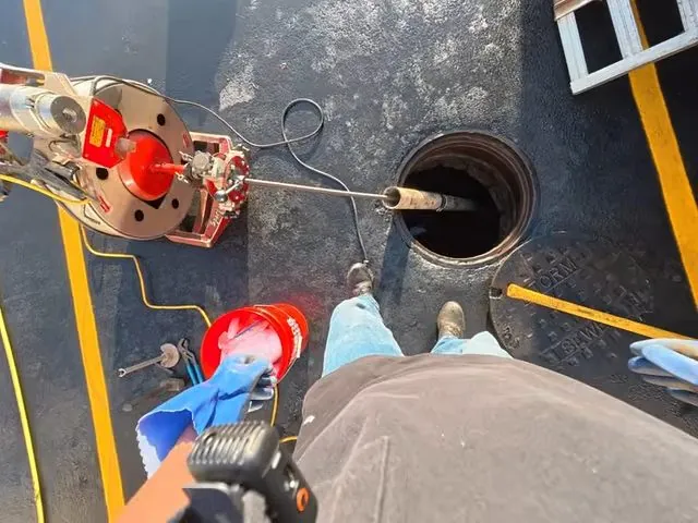 Drain cleaning machine on a floor with its cable running into an open floor cleanout.
