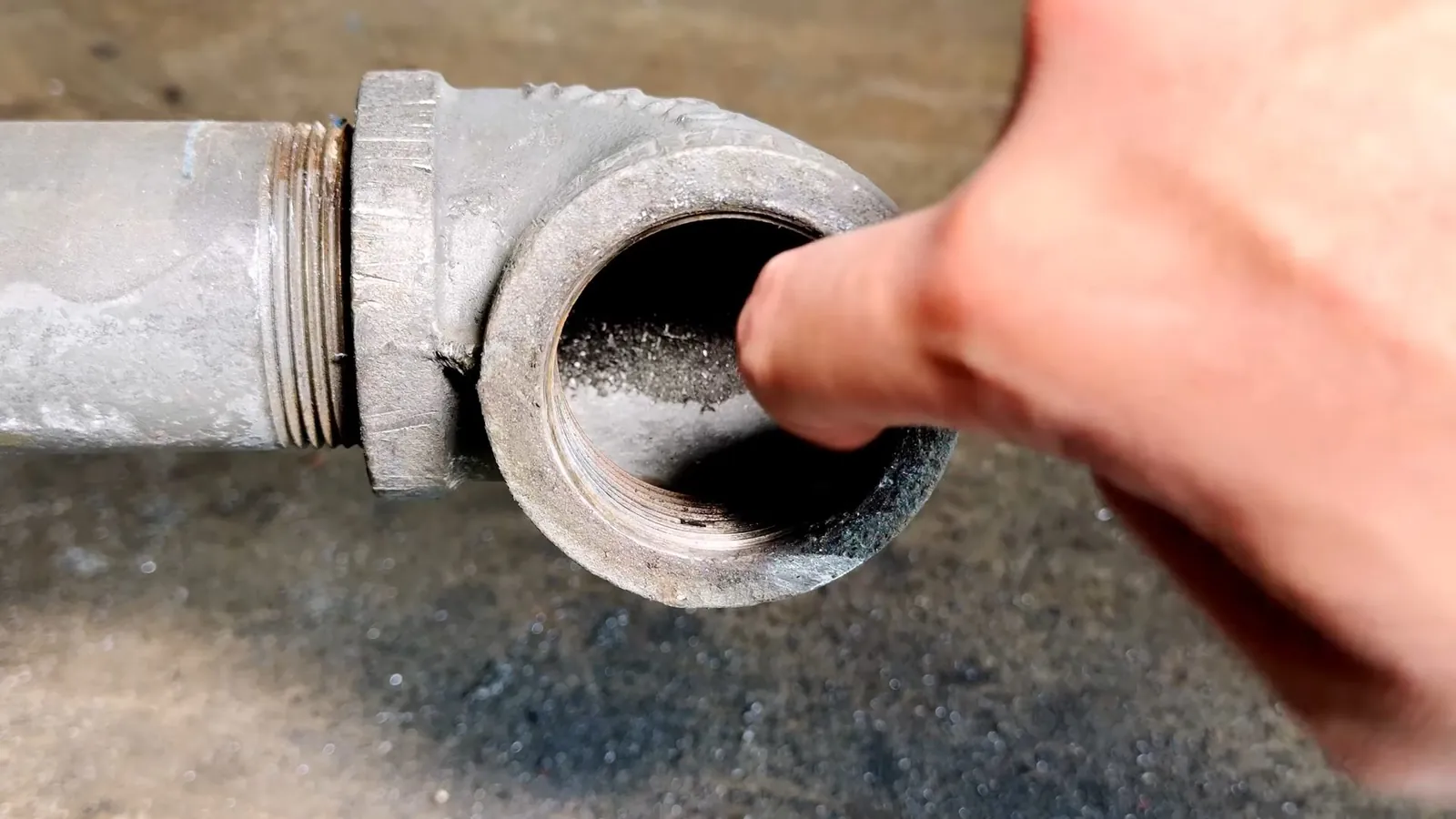 Finger pointing into the open end of a galvanized steel elbow caked with debris.