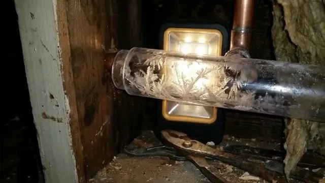 Pipe in a dark wall cavity with frost crystals visible inside it, lit by a work light.