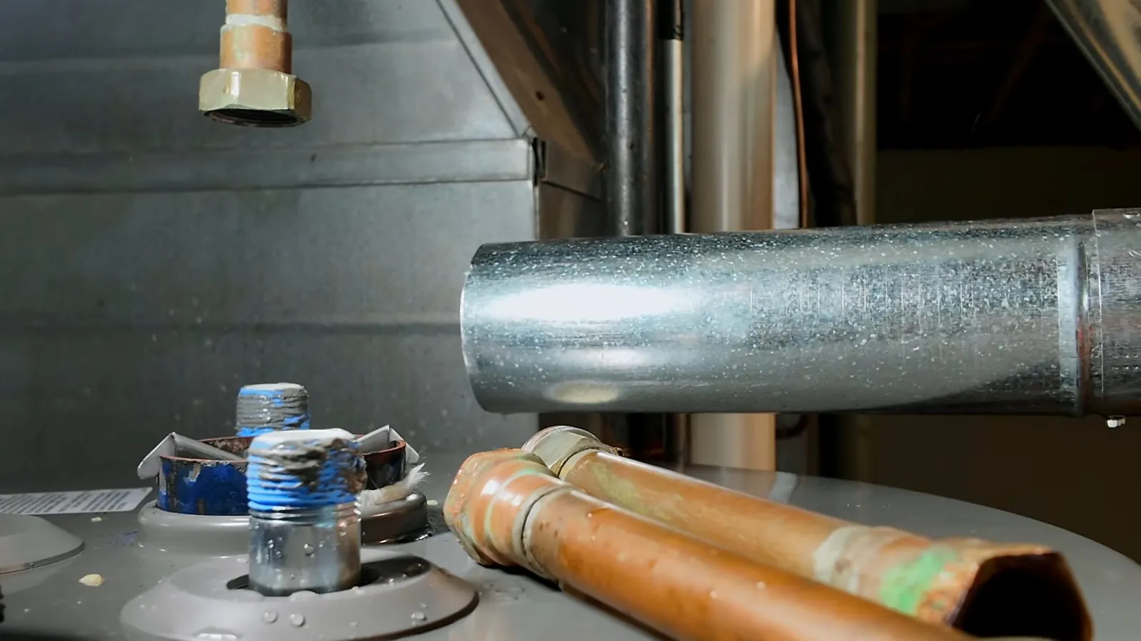 Galvanized flue pipe and two copper supply lines above the top of a tank water heater with blue-capped fittings.