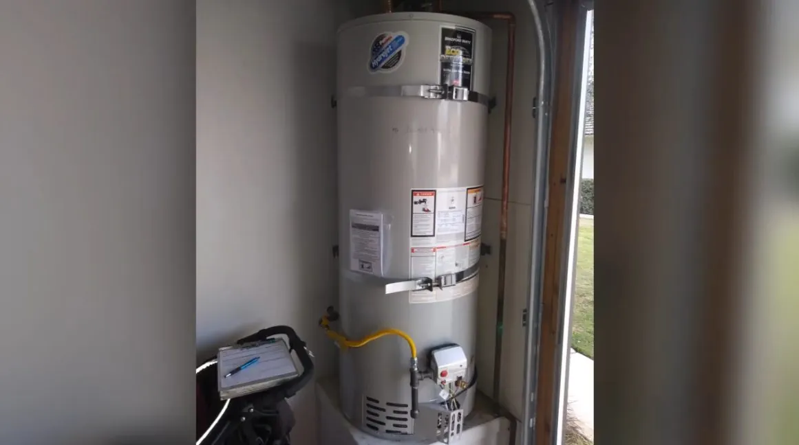 Gas tank water heater with a control and cord at its base inside a utility closet.