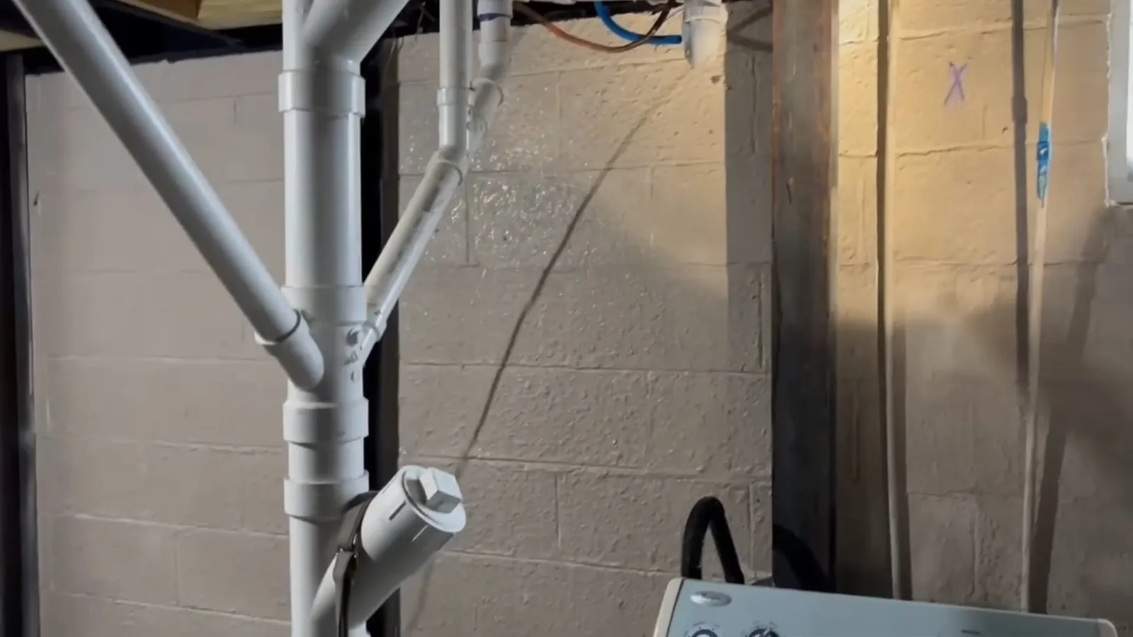 Gray PVC drain pipes rising along a concrete block basement wall.
