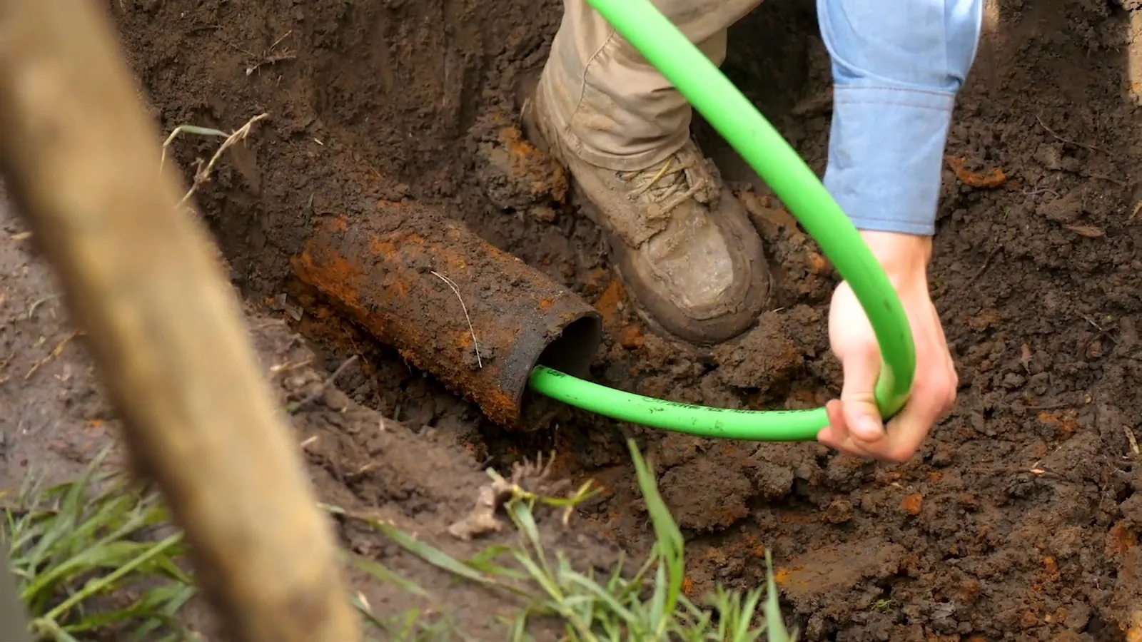 Worker feeding a green line into the open end of a rusted pipe in a hole in the lawn.