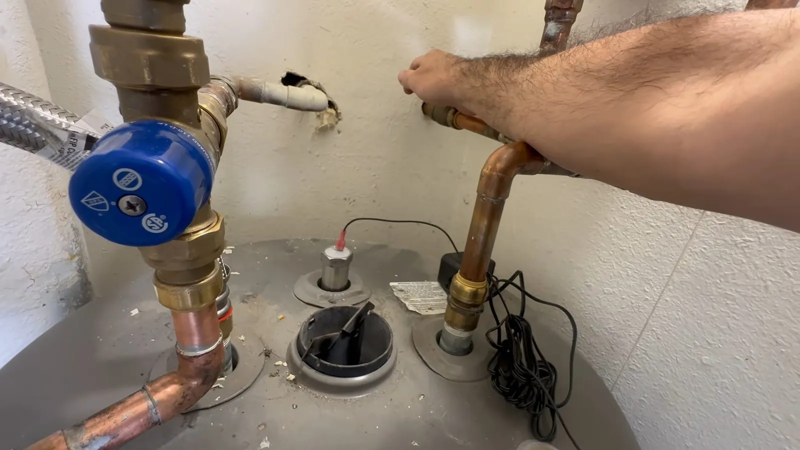 Hand tightening a copper elbow beside blue shutoff and relief valves on top of a tank water heater.