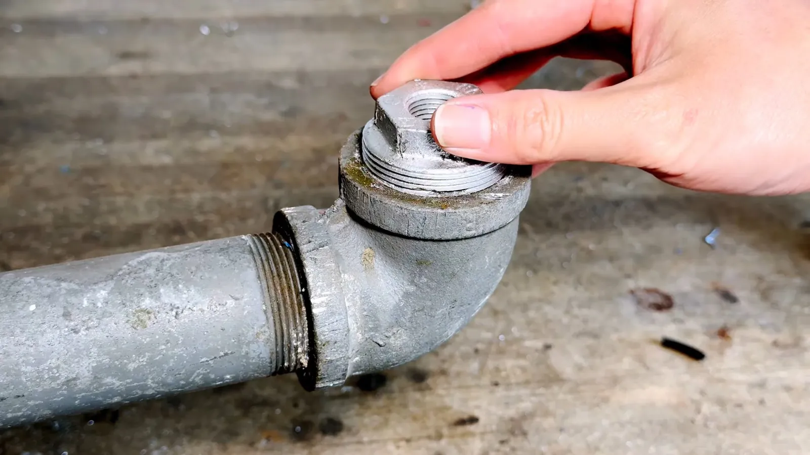 Hand unscrewing the cap of a galvanized cleanout fitting on a gray pipe.