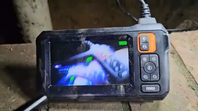 Handheld inspection camera monitor showing a pipe interior on a ledge.