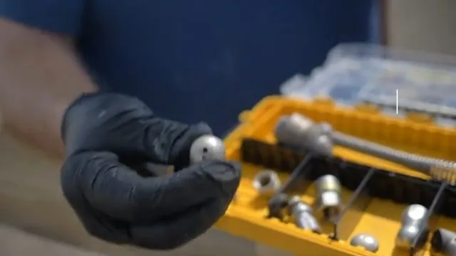 Gloved hand holding a jetting nozzle above a tray of other nozzle heads.