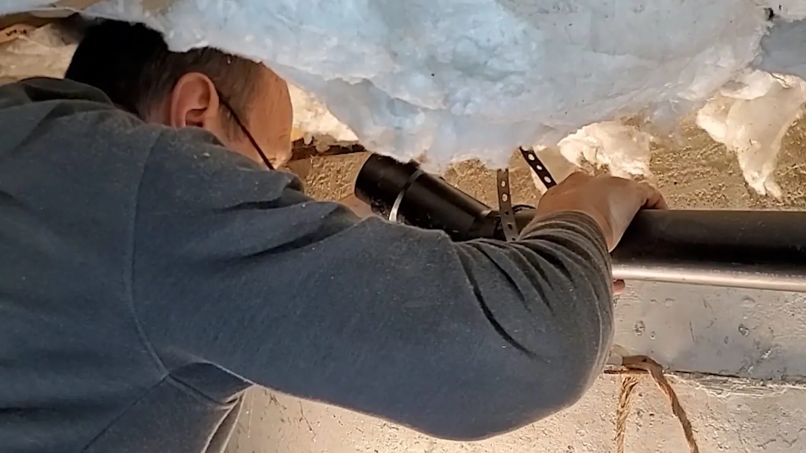 Man reaching into a ceiling space past insulation to a pipe.