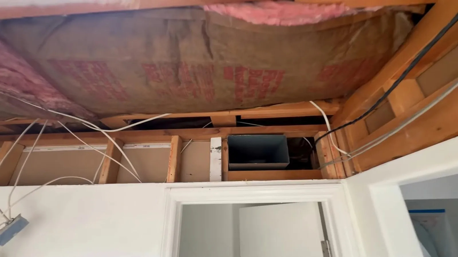Open ceiling with pink insulation exposed between joists after the drywall was removed.