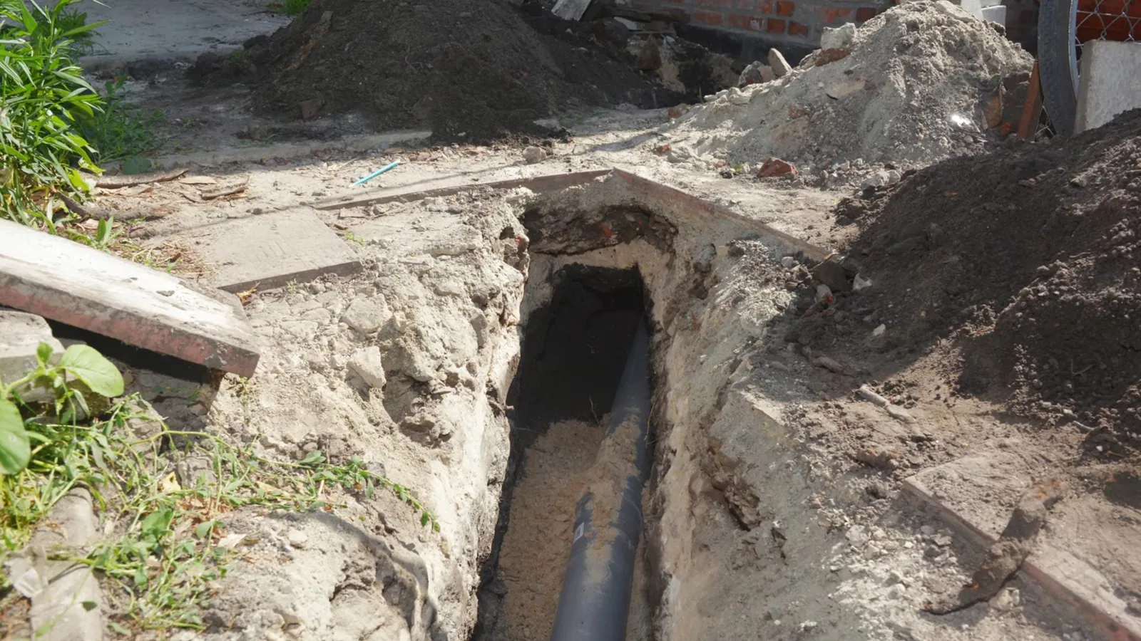 Open trench in a lawn exposing a dark pipe beside piles of soil.