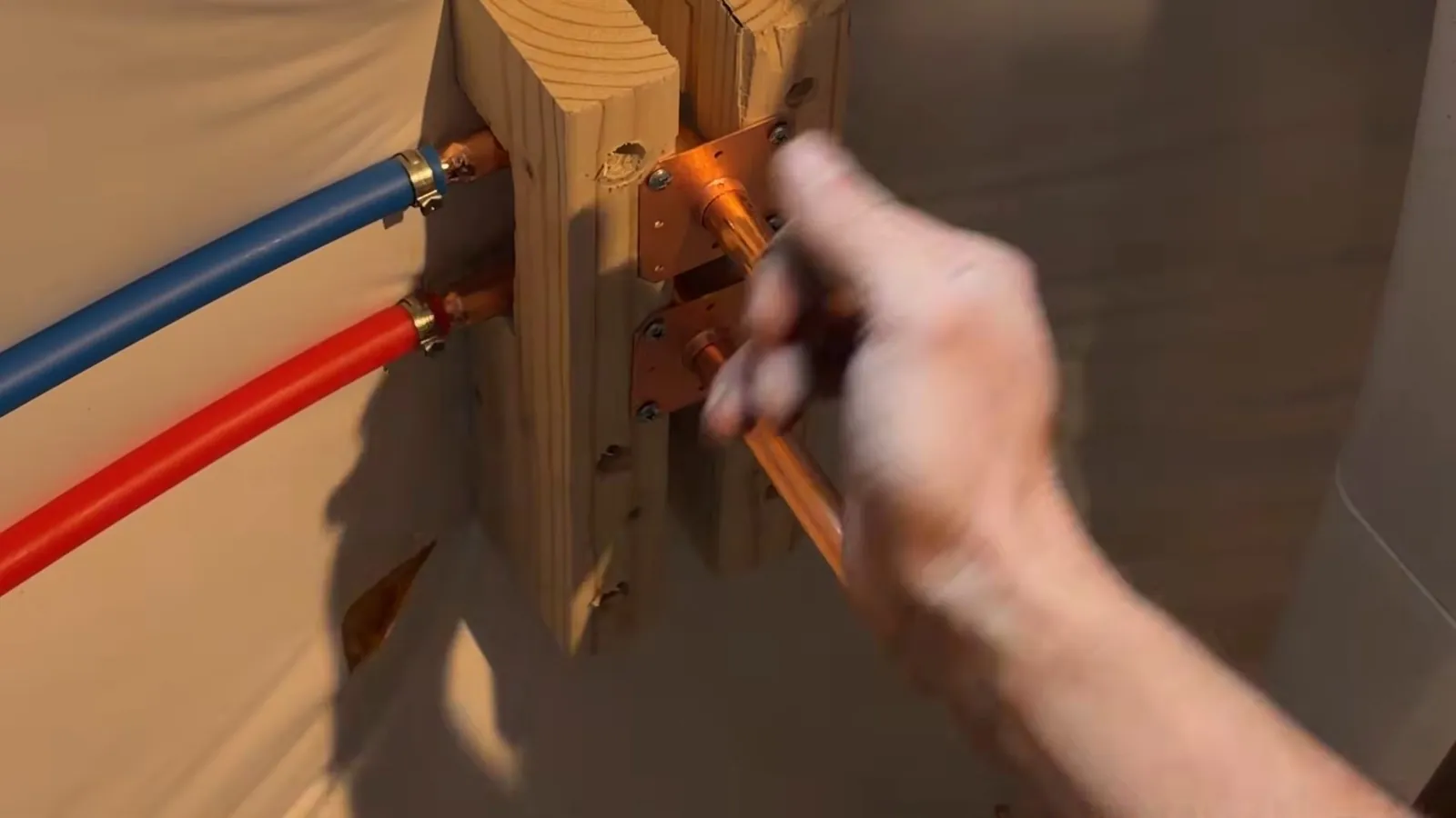 Hand tightening a copper manifold with red and blue PEX lines mounted on a wood backer.