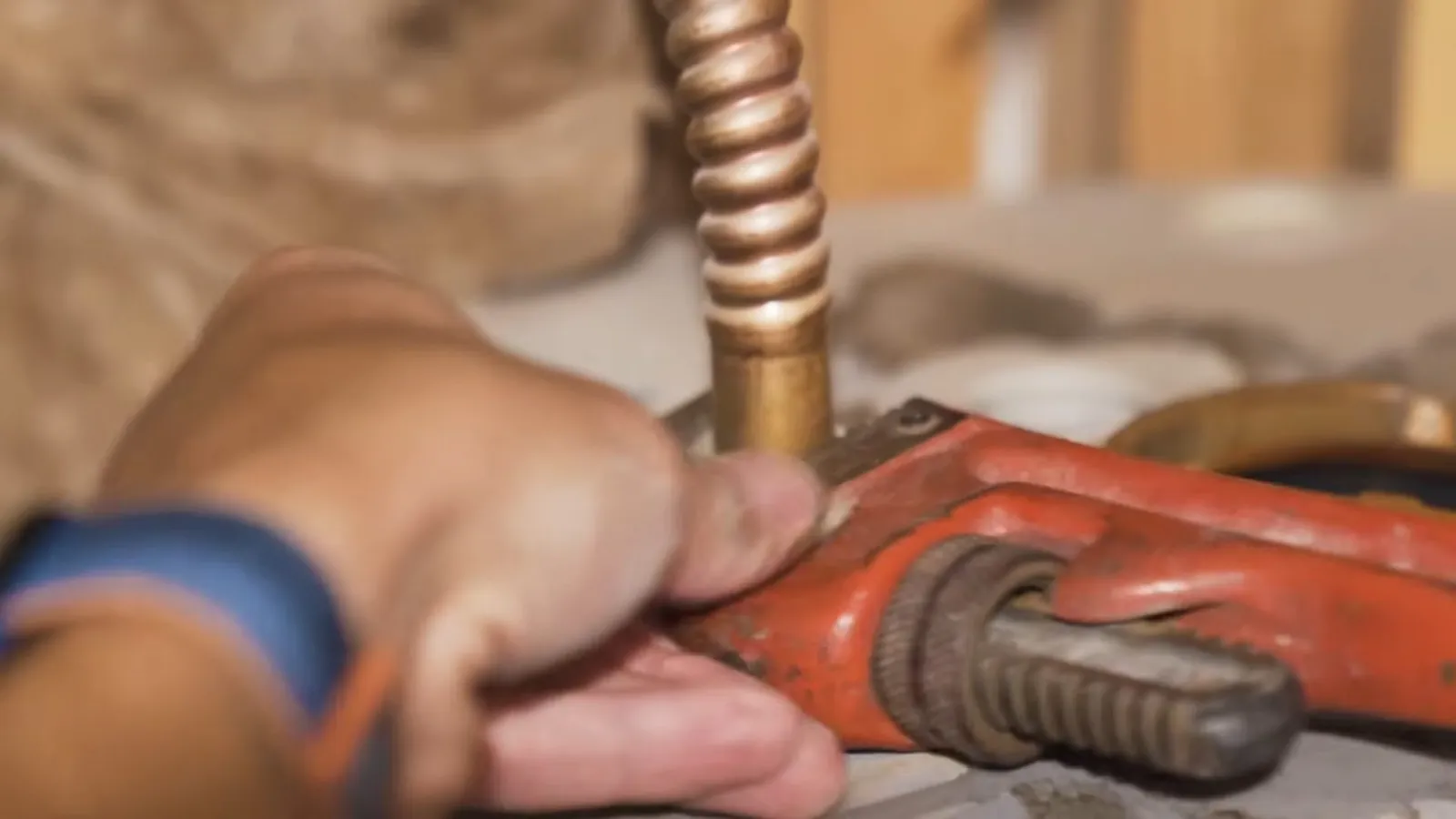 Hand using an orange pipe wrench on a corrugated gas connector fitting.