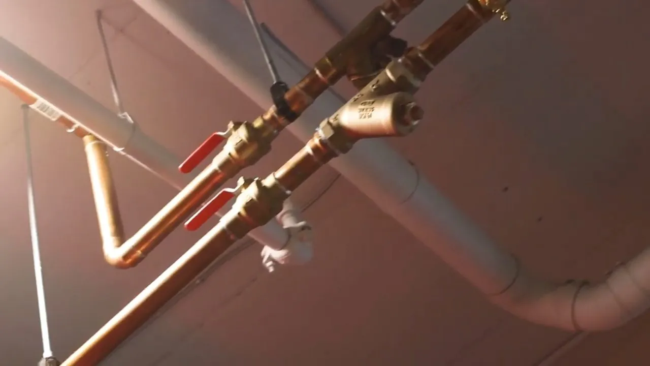 Two red-handled brass valves on copper supply pipes running along a basement ceiling.