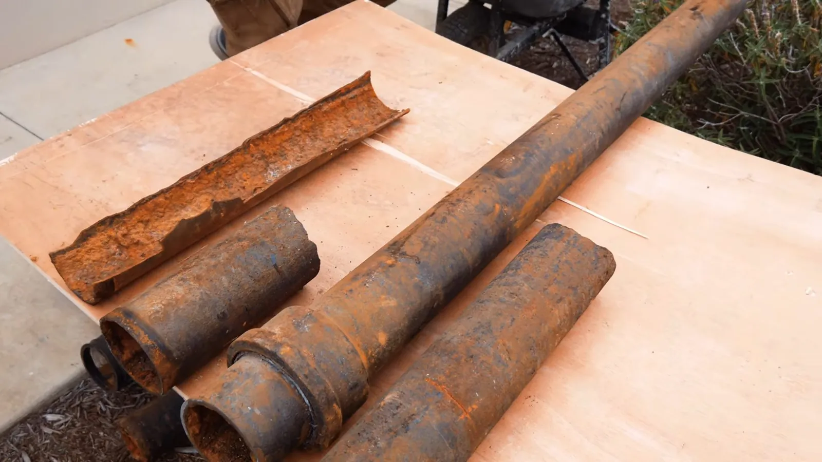 Three cut sections of heavily rusted steel pipe lying on a plywood sheet.