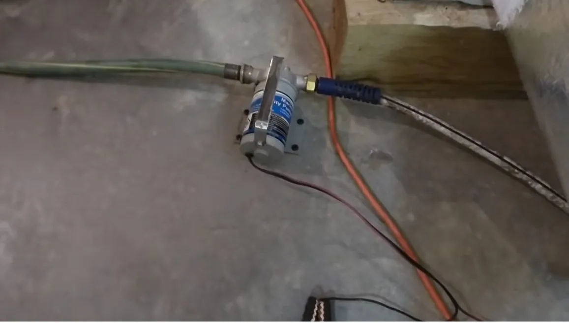 Small blue pump with a green hose and an orange power cord on a gray basement floor.