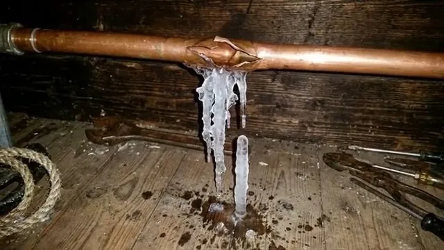 Copper pipe split open along its length with icicles hanging from it.