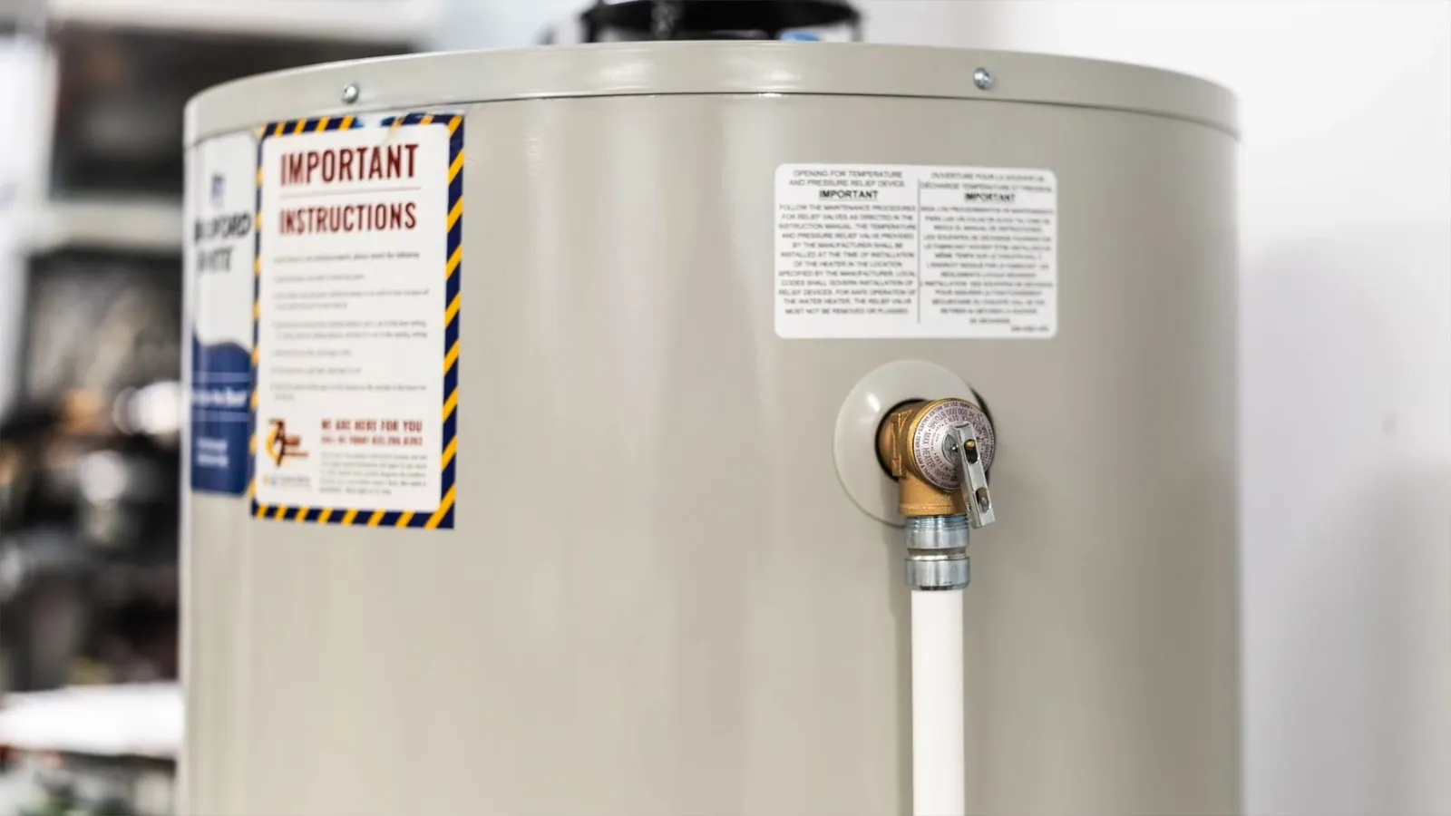 Tank water heater with a yellow warning label and a relief valve fitted with a white pipe.