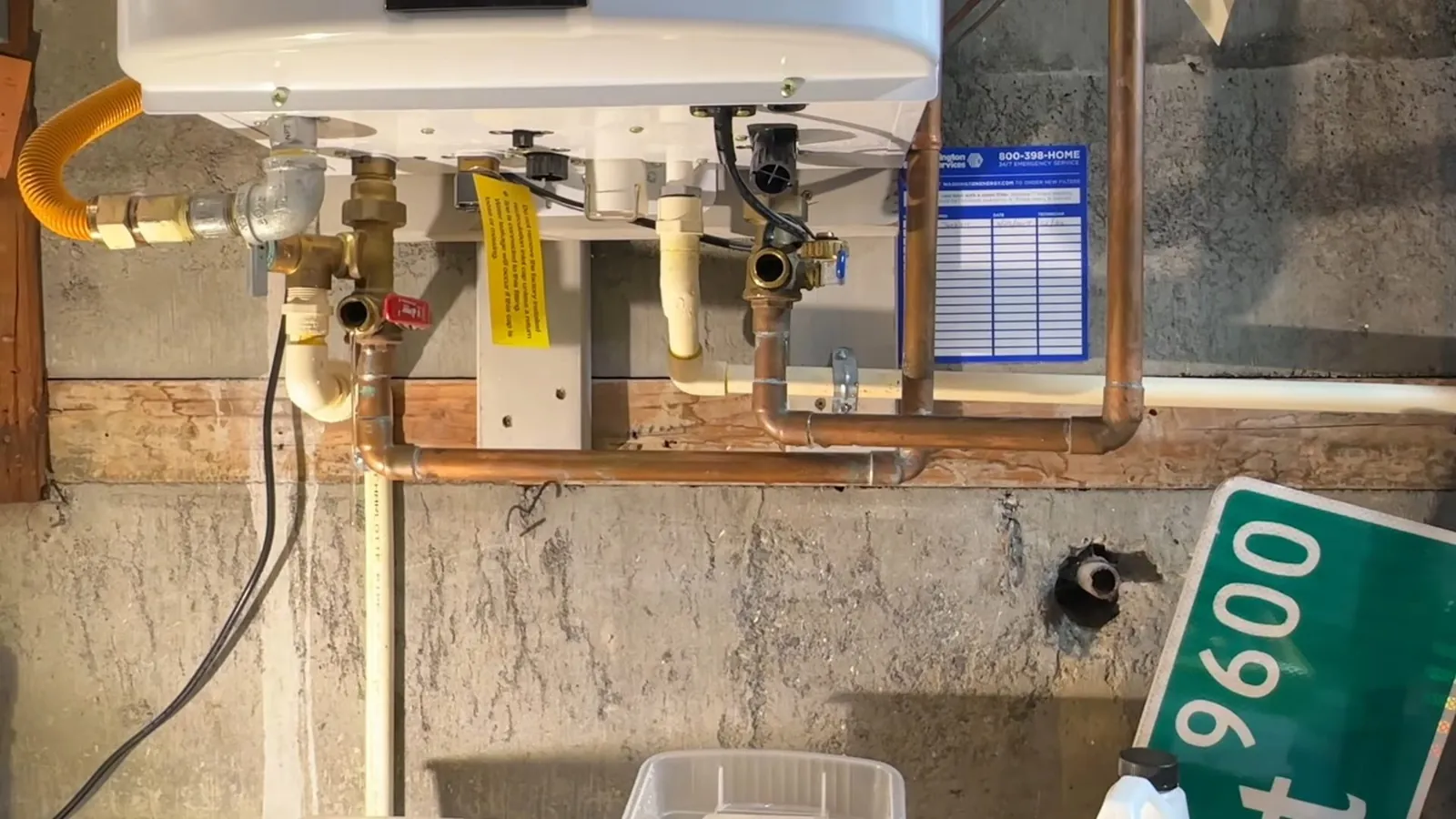 Tankless water heater on a concrete wall with copper piping, valves and a yellow gas tag.