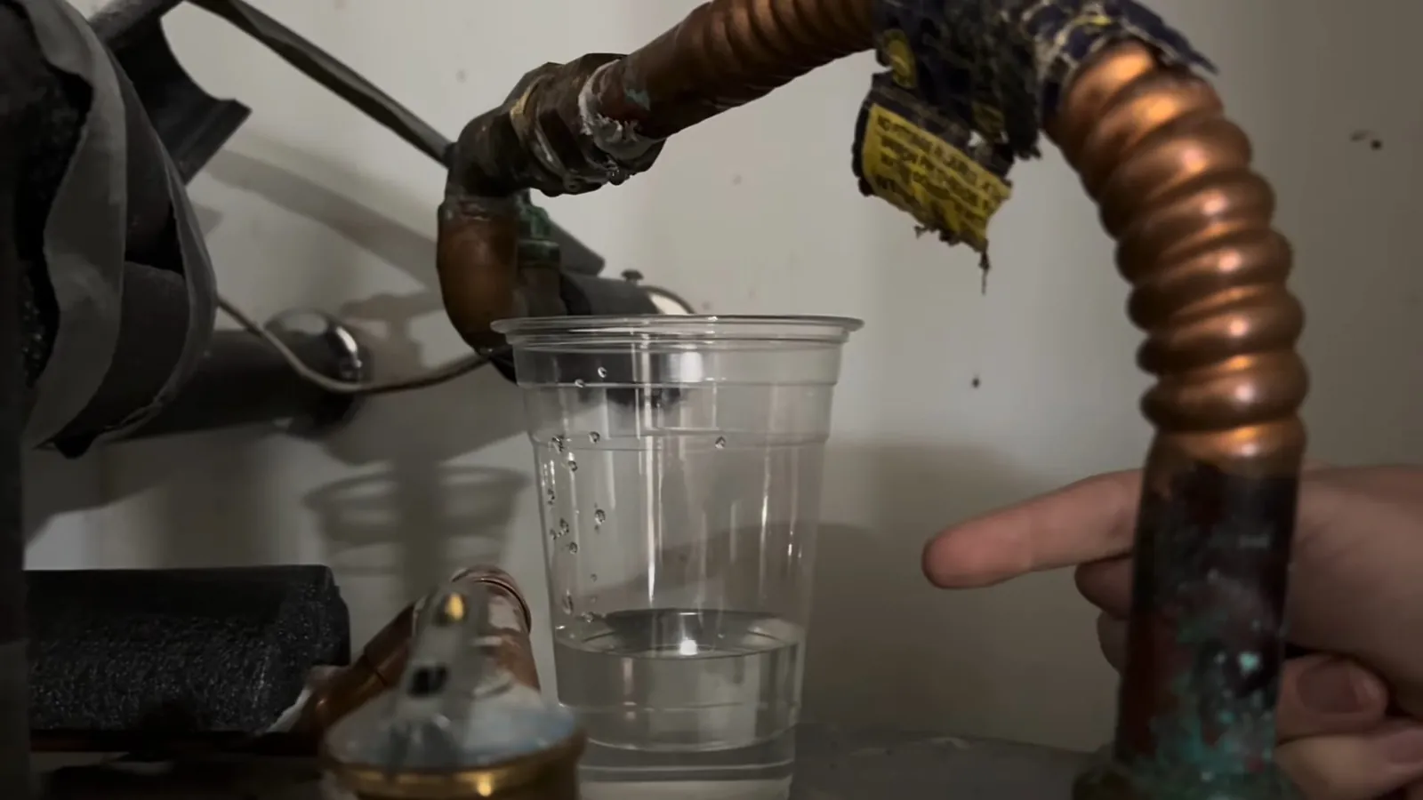 Copper discharge pipe from a water heater relief valve with a clear cup held beneath it.