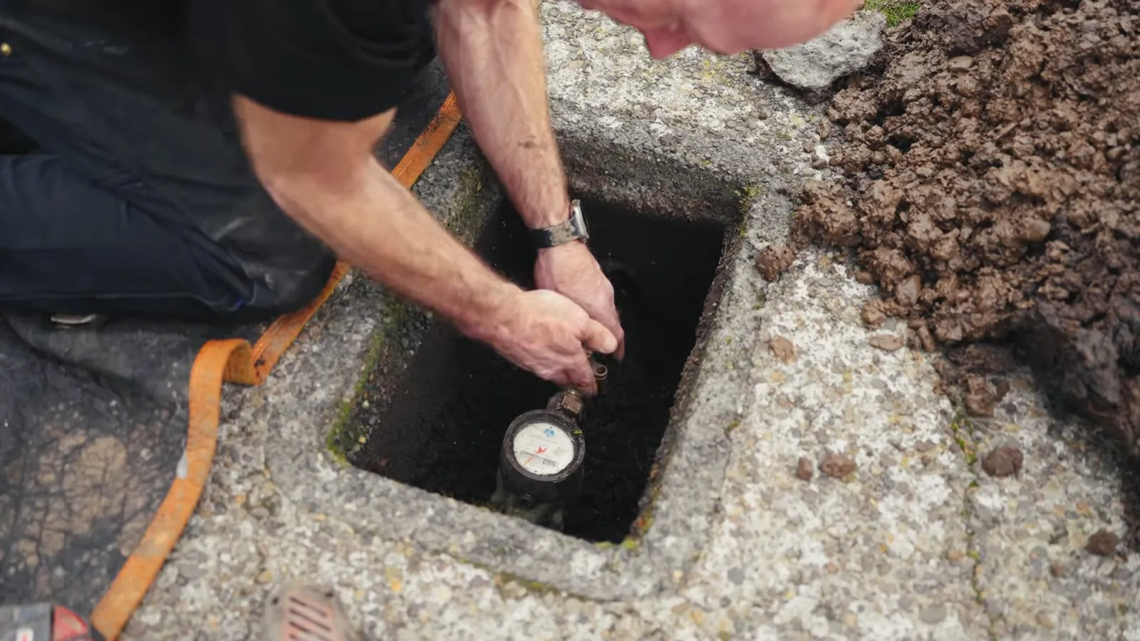 Man kneeling beside an open ground box with his hand on the water meter inside.