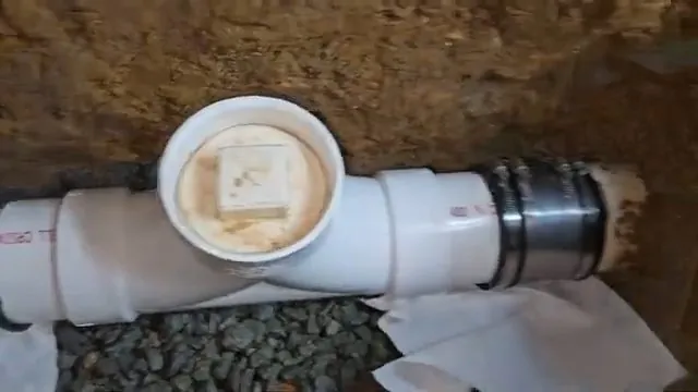 White PVC pipe with a capped cleanout tee and a rubber coupling laid in a trench over gravel.