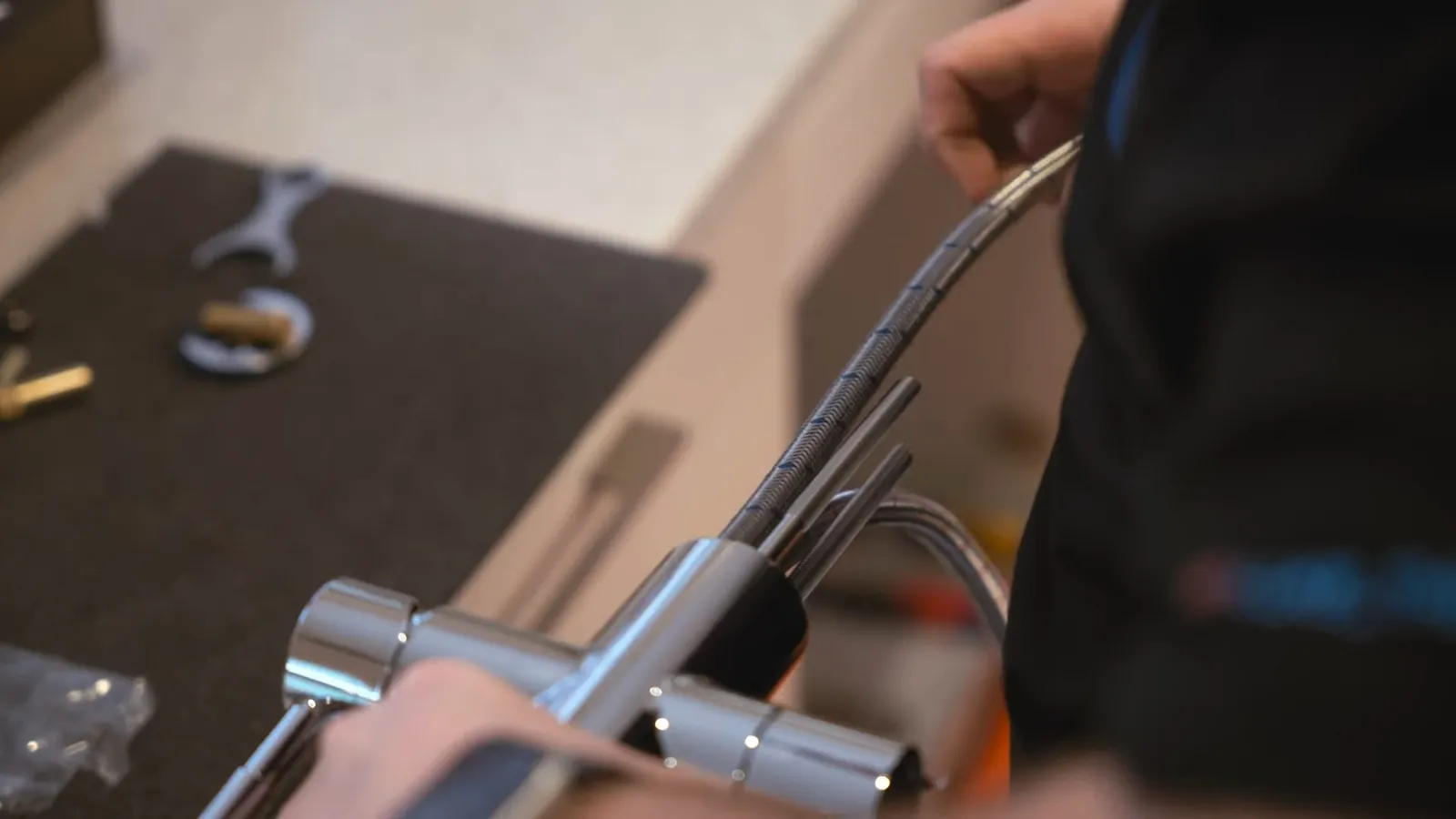 Man installing a chrome faucet from beneath a counter with a wrench lying beside it.