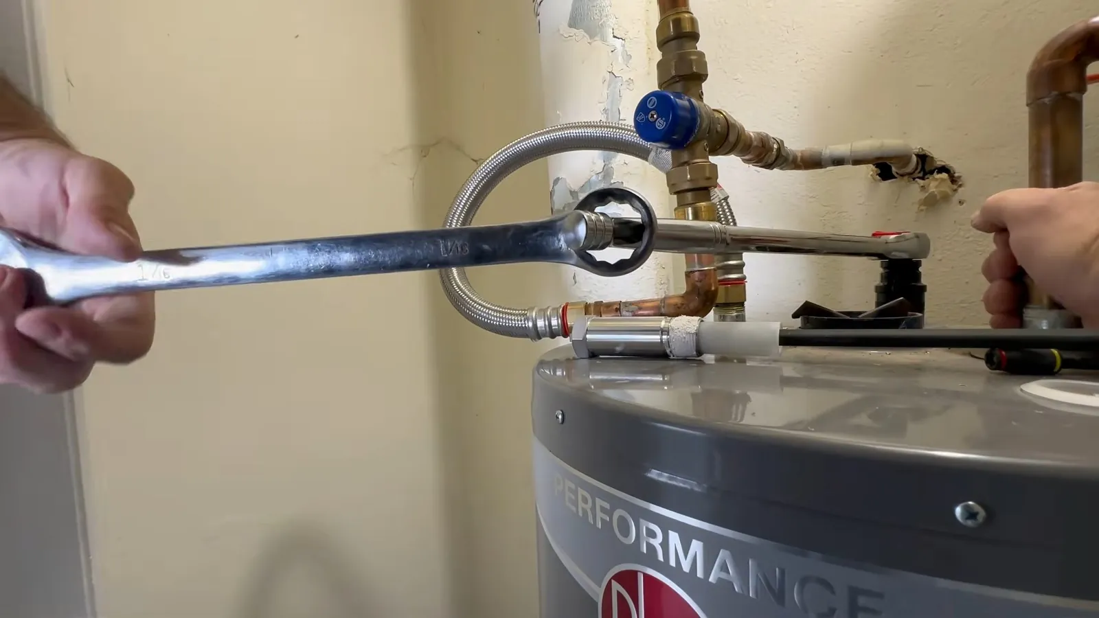 Wrench tightening a flexible connector on top of a new tank water heater.